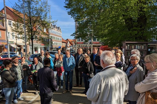 Menschen stehen im Halbkreis am Kirchplatz in Vorsfelde und hören einer Mitarbeiterin des Zentrenbüros zu.