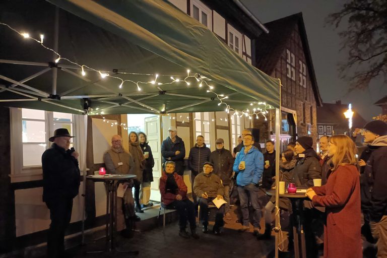 Menschen stehen vor dem Zentrenbüro Fallersleben. Es ist mit Pavillon und Lichterketten dekoriert. Vor ihnen spricht Ortsbürgermeister Schlichting.