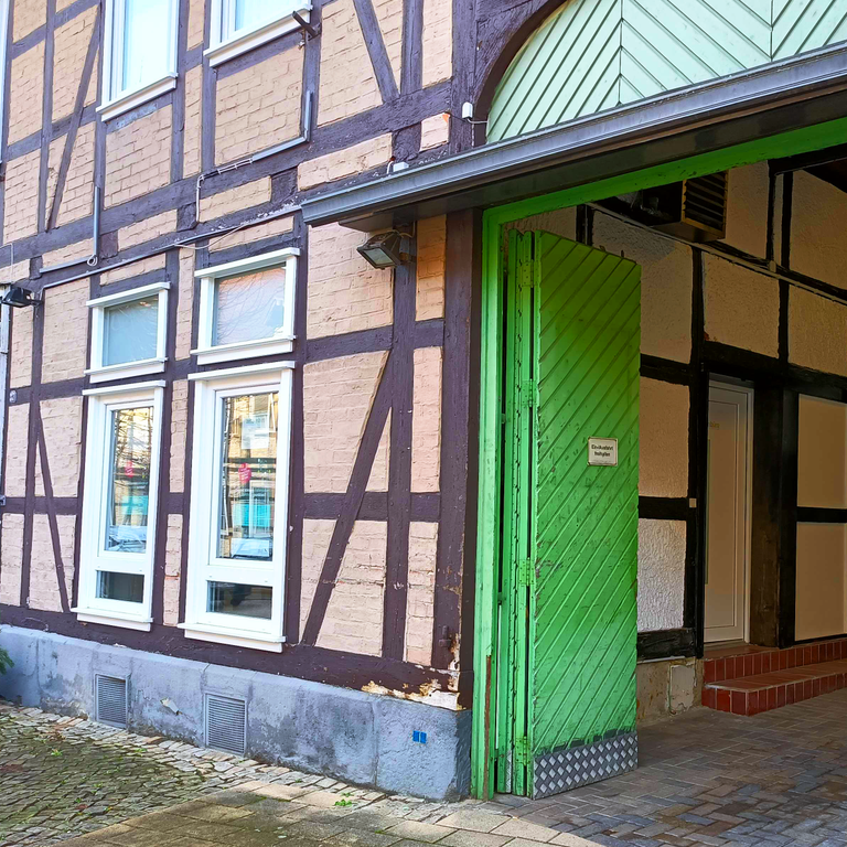 Fachwerkhaus in der Langen Straße. Hinter einem offenstehenden grünen Einfahrtstor sieht man die Eingangstür des Zentrenbüros.